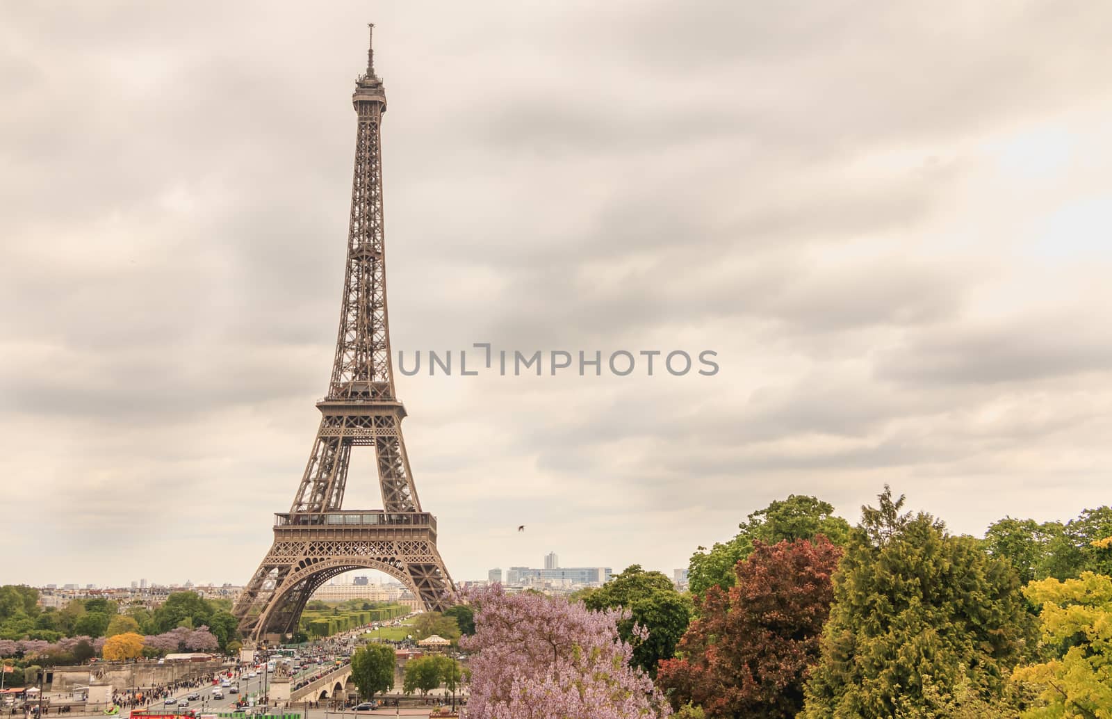 PARIS, FRANCE - May 08, 2017 : wide shot of the Eiffel Tower in Paris with tourists walking in bad weather on a spring day
