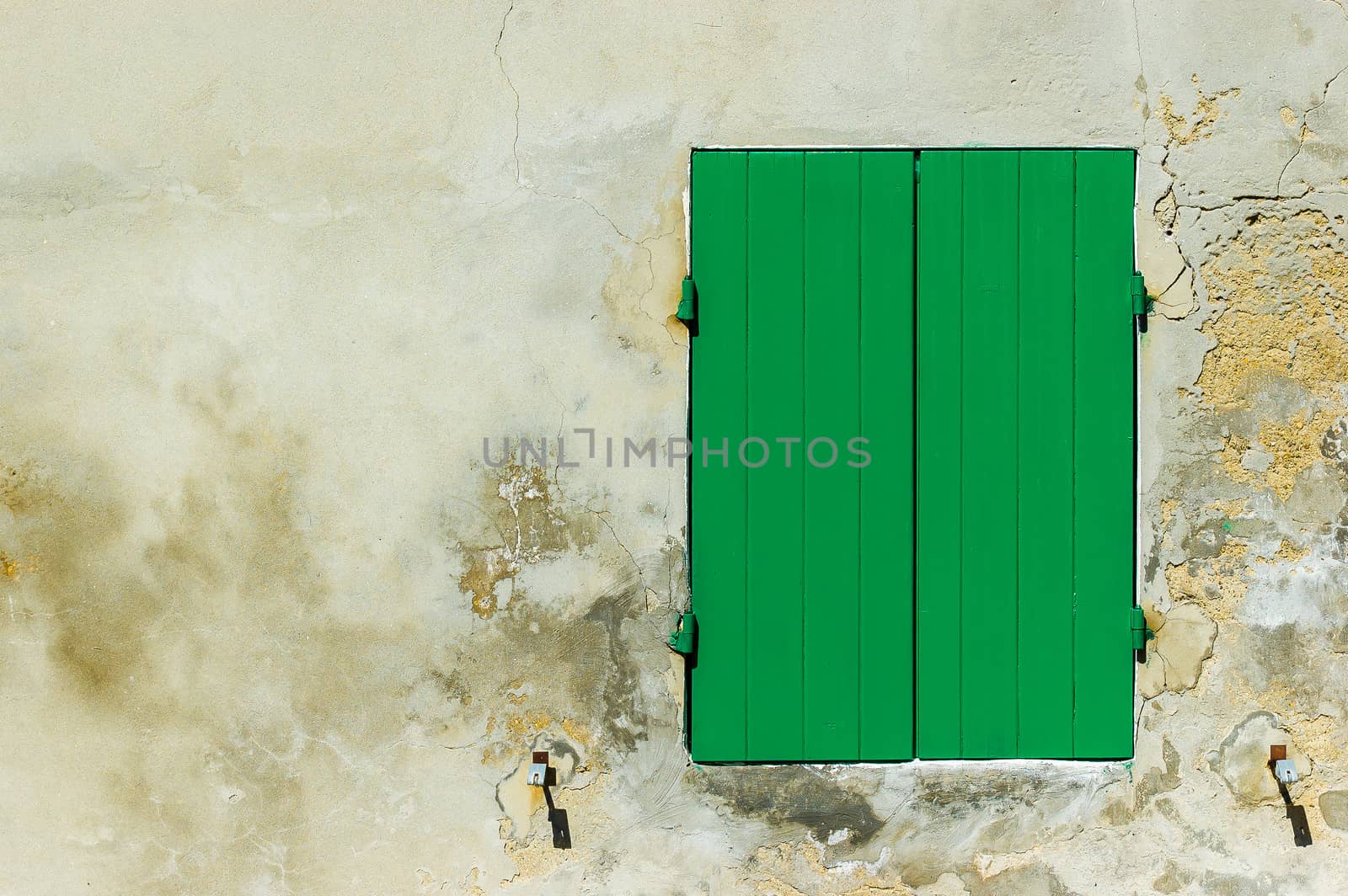 A closed green shutter and an old concrete wall illuminated by a strong sun light