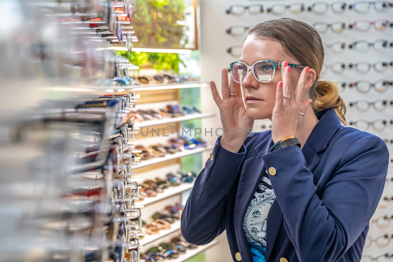 A young attractive woman in an optics store tries on new glasses. copy space by Edophoto