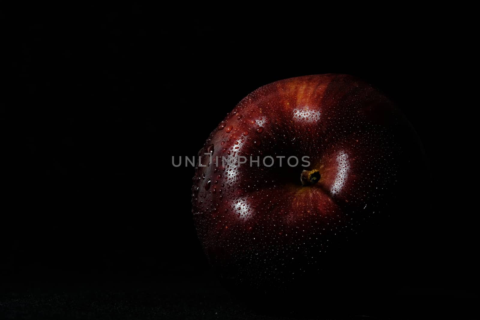 Close up fresh red Apple with water droplet isolated on black background – low key macro shoot