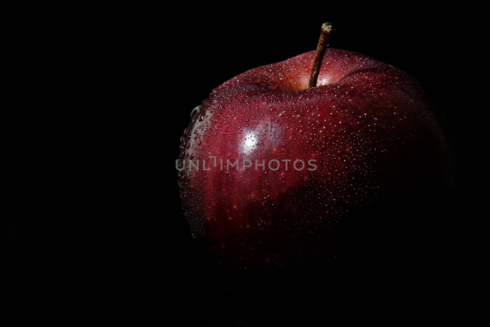 Close up fresh red Apple with water droplet isolated on black background – low key macro shoot