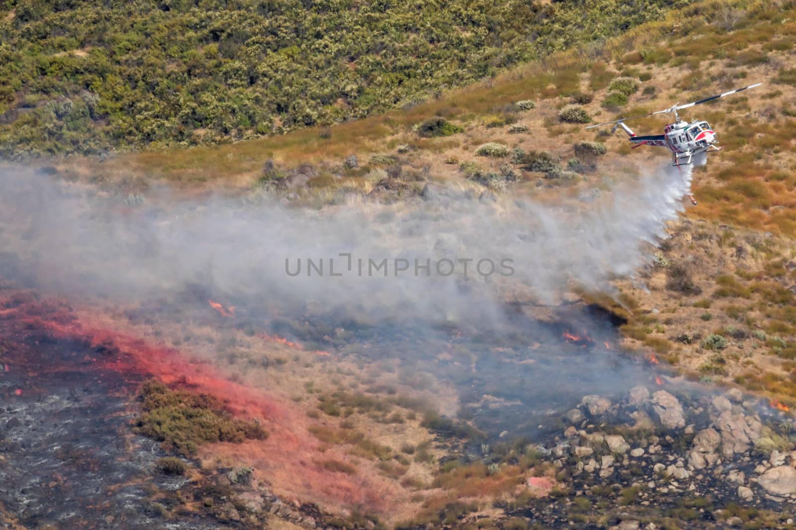 Winchester, CA USA - June 14, 2020: Cal Fire helicopter drops water on a dry hilltop wildfire near Winchester, California. by Feverpitched