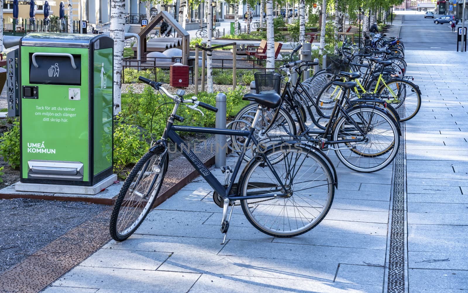 UMEA, SWEDEN - JUNE 10, 2020: A lot of bikes parked in long row on the street close to green recycling bin and small play park for children, central part of Umea city, Vasterbotten. Nice summer day by skydreamliner