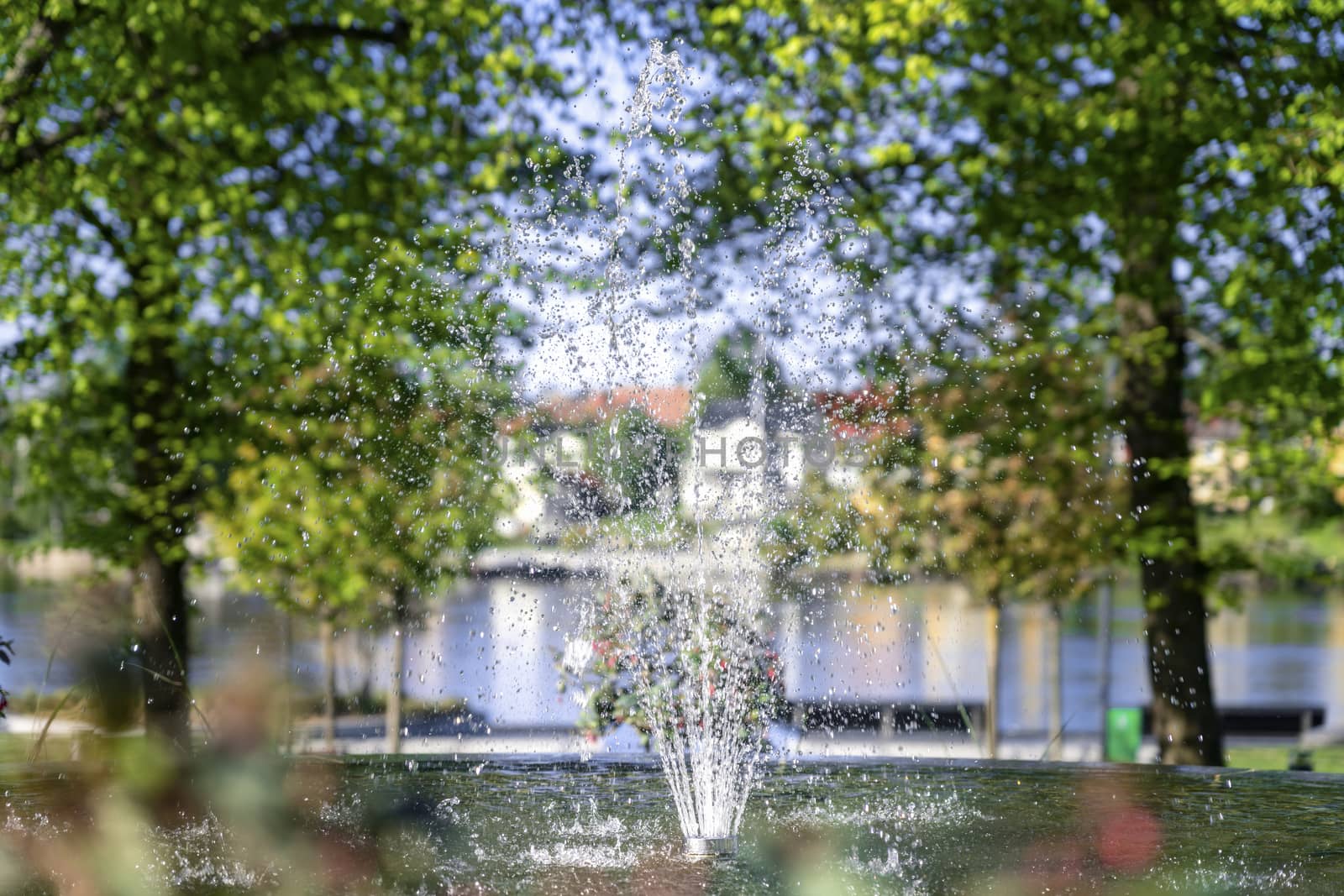 Beautiful close up photo of fresh fontain with water splashing, sunny summer blurry background with trees, river and houses, Radhusparken park, Umea Vasterbotten Sweden by skydreamliner