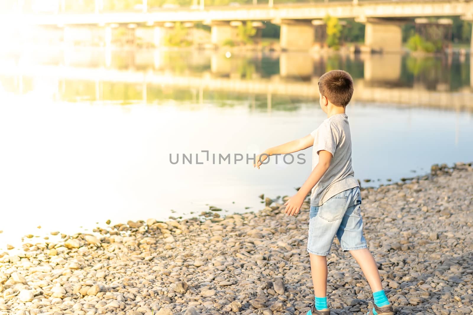 a child, a teenager, on a stony shore throws stones into the river by jk3030