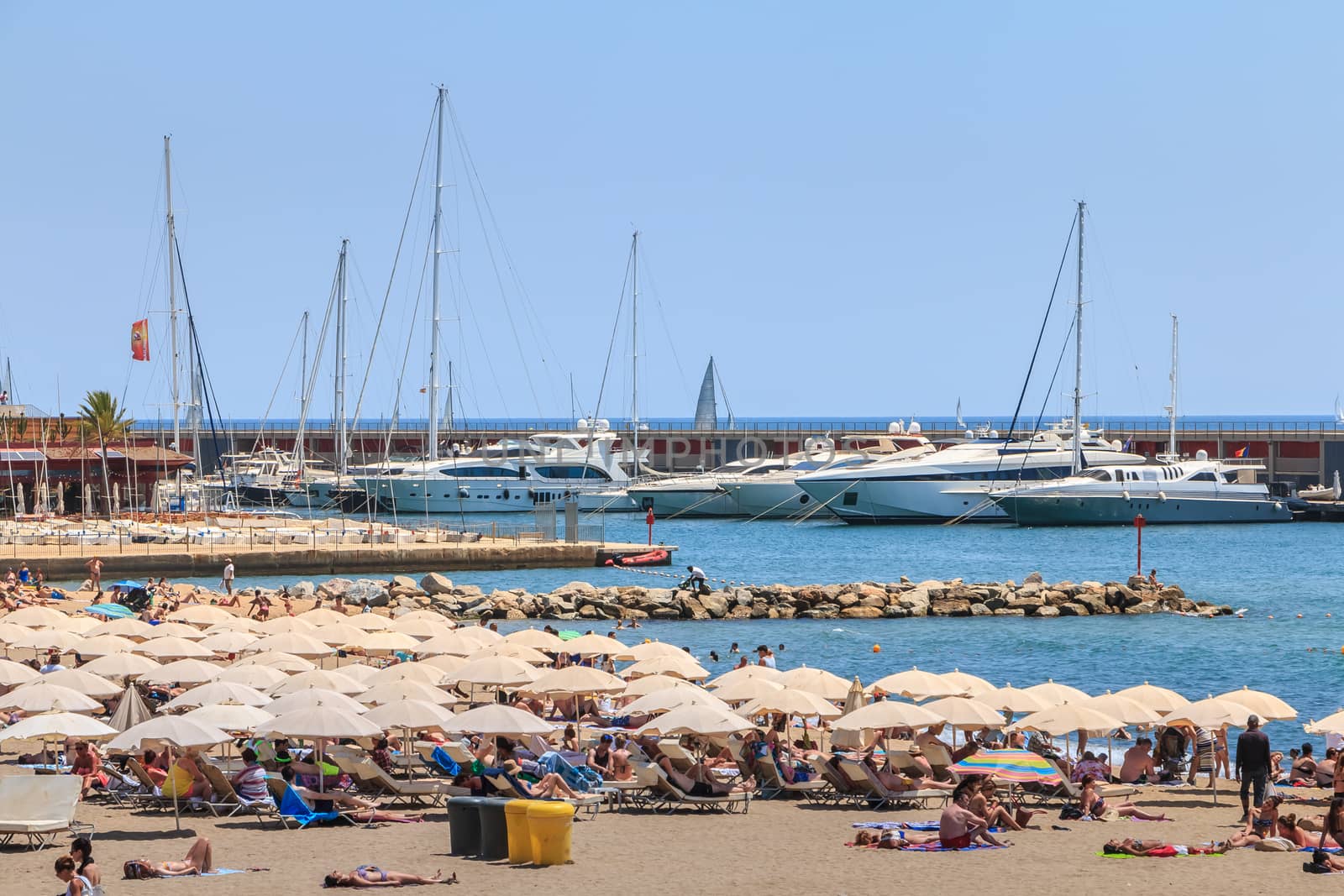 BARCELONA, SPAIN - June 21, 2017 : during the summer, people are resting on the beach in front of the Olympic port where are moored very luxurious boats