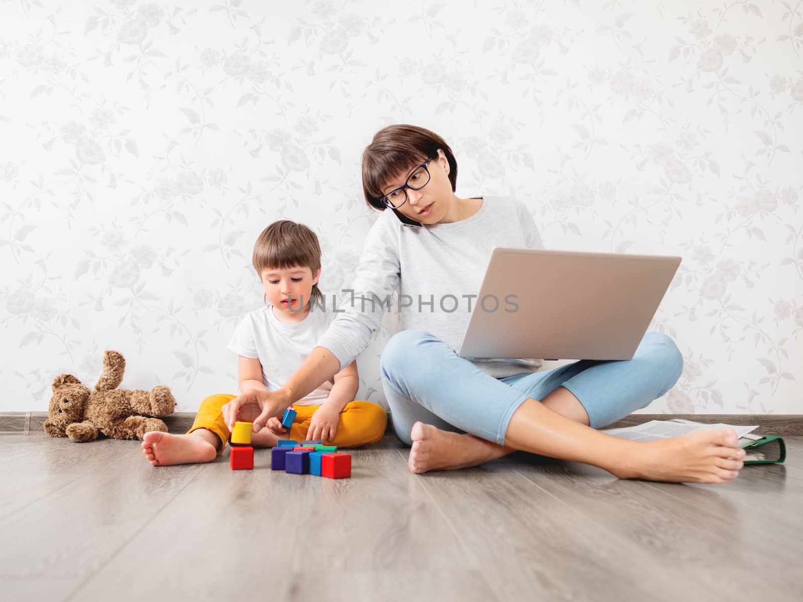 Mom and son at home quarantine because of coronavirus COVID19. Mother works remotely with laptop, son plays with toy blocks. Self isolation at home.