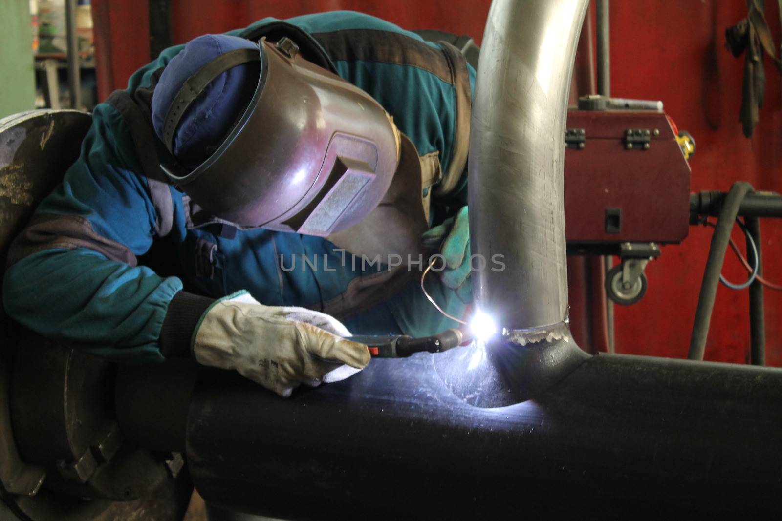 Welder Worker Performs Jump Welding. Worker Welder Performs Arc-Welding Process of Metal Structures. Flying Sparks From the Welding Machine. Welder Welds Metal Profiles for Second Floor Indoors