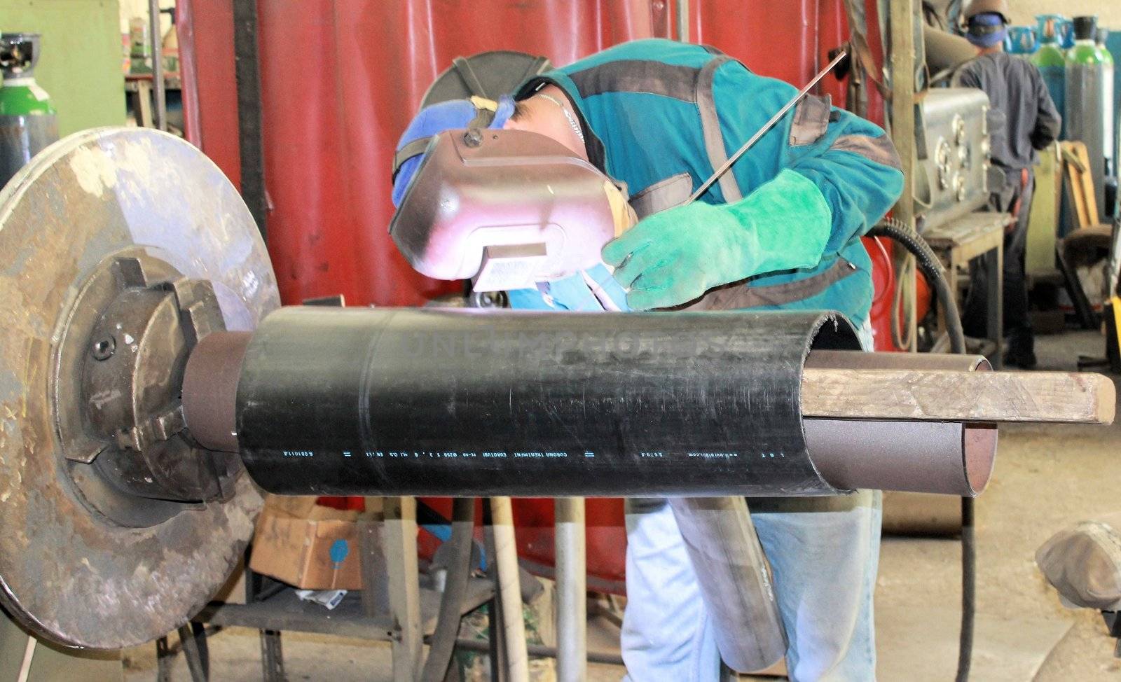 The welder is assembling valve to the pipe line with Tungsten Inert Gas Welding process (TIG). The welder wears protective equipment with a welding mask and heat resistant gloves.