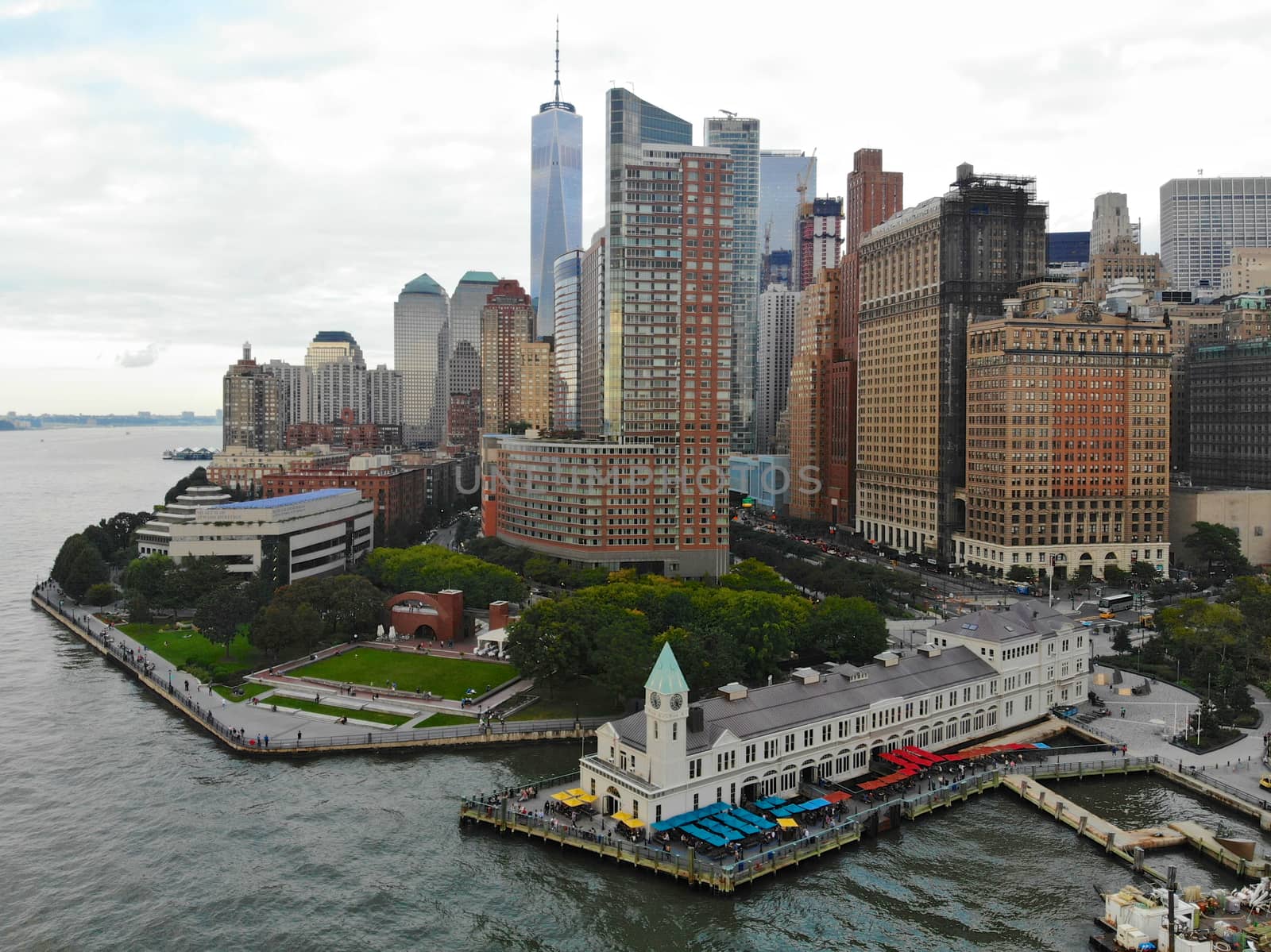 Aerial view of Battery Park pier A leading to Liberty Island, people can be seen waiting in line for boarding as well as looking at Liberty Island located opposite to the docks. October, 22nd, 2019
