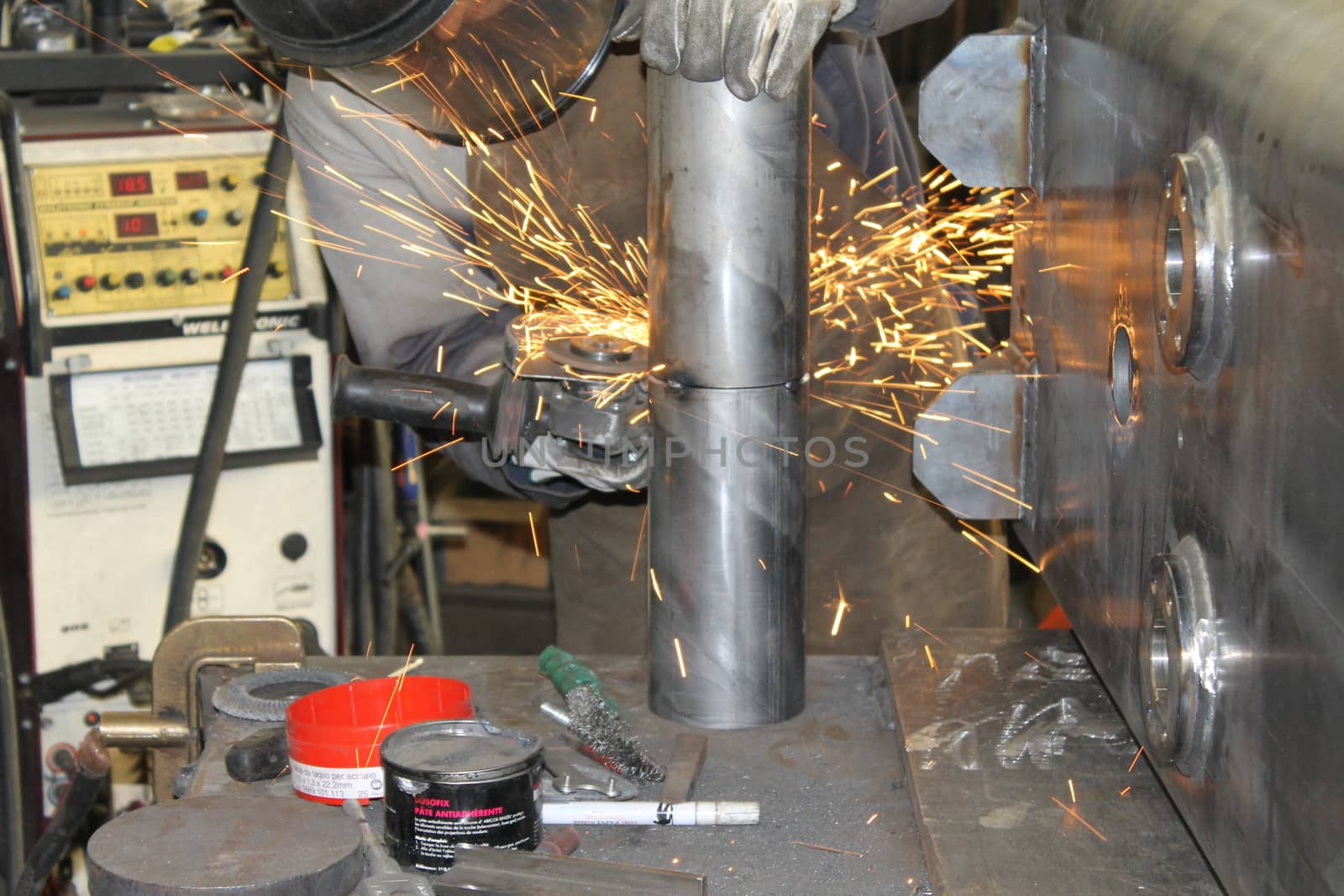 craftsman with working gloves cutting an iron bar with the electric angle grinder which sprays many hot sparks in the dark workshop, dangerous work, copy space