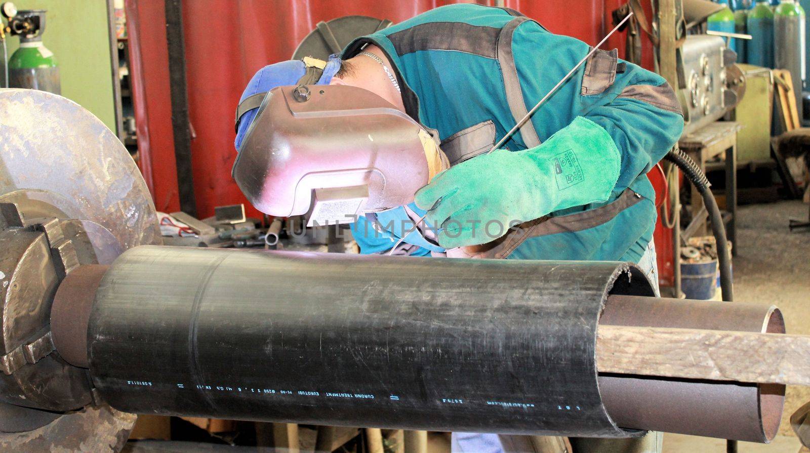 The welder is assembling valve to the pipe line with Tungsten Inert Gas Welding process (TIG). The welder wears protective equipment with a welding mask and heat resistant gloves.