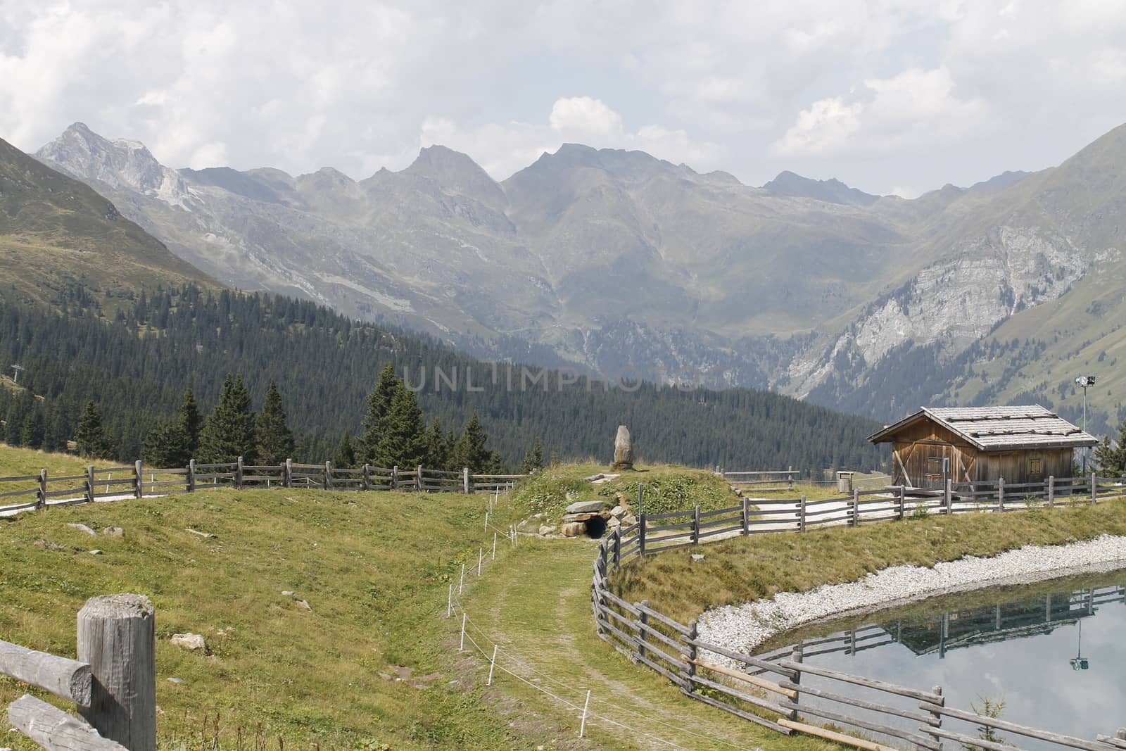 Scenic view to small alpine lake and big mountains with glacier in sunlight. Awesome green landscape with blue mountain lake among mosses in green highland valley in sunny day. Wonderful scenery.