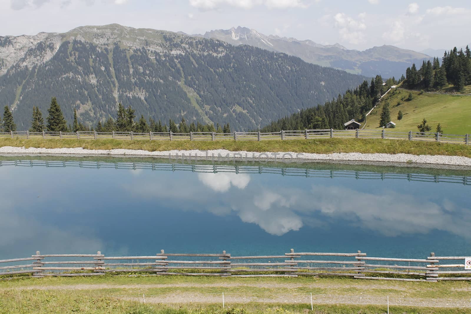 Scenic view to small alpine lake and big mountains with glacier in sunlight. Awesome green landscape with blue mountain lake among mosses in green highland valley in sunny day. Wonderful scenery.