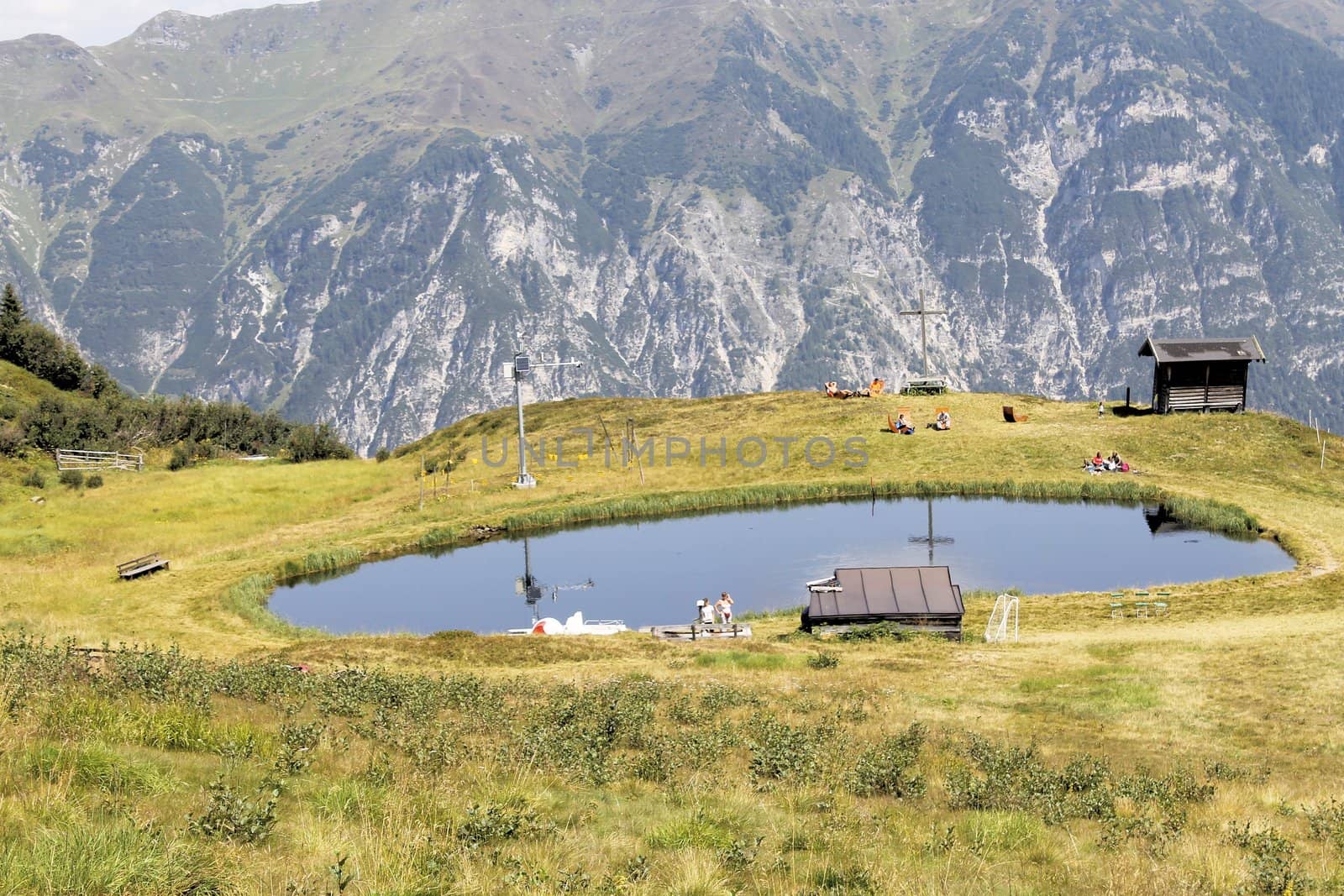 Scenic view to small alpine lake and big mountains with glacier in sunlight. Awesome green landscape with blue mountain lake among mosses in green highland valley in sunny day. Wonderful scenery.