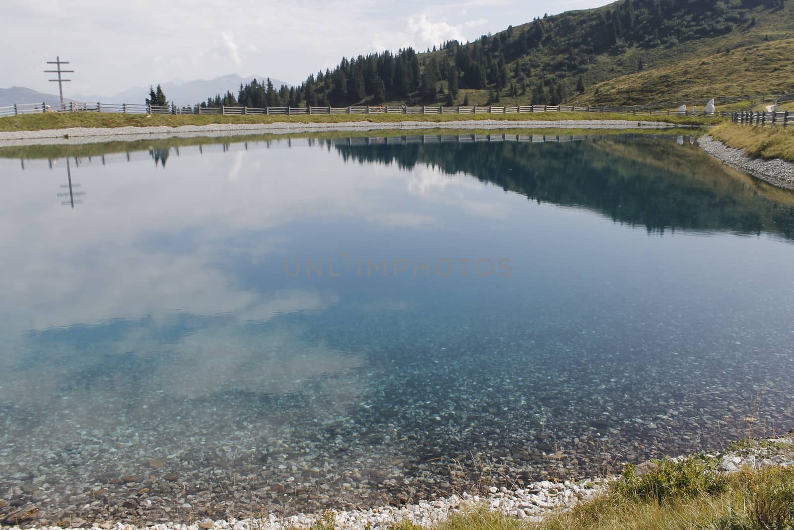 Scenic view to small alpine lake and big mountains with glacier in sunlight. Awesome green landscape with blue mountain lake among mosses in green highland valley in sunny day. Wonderful scenery.