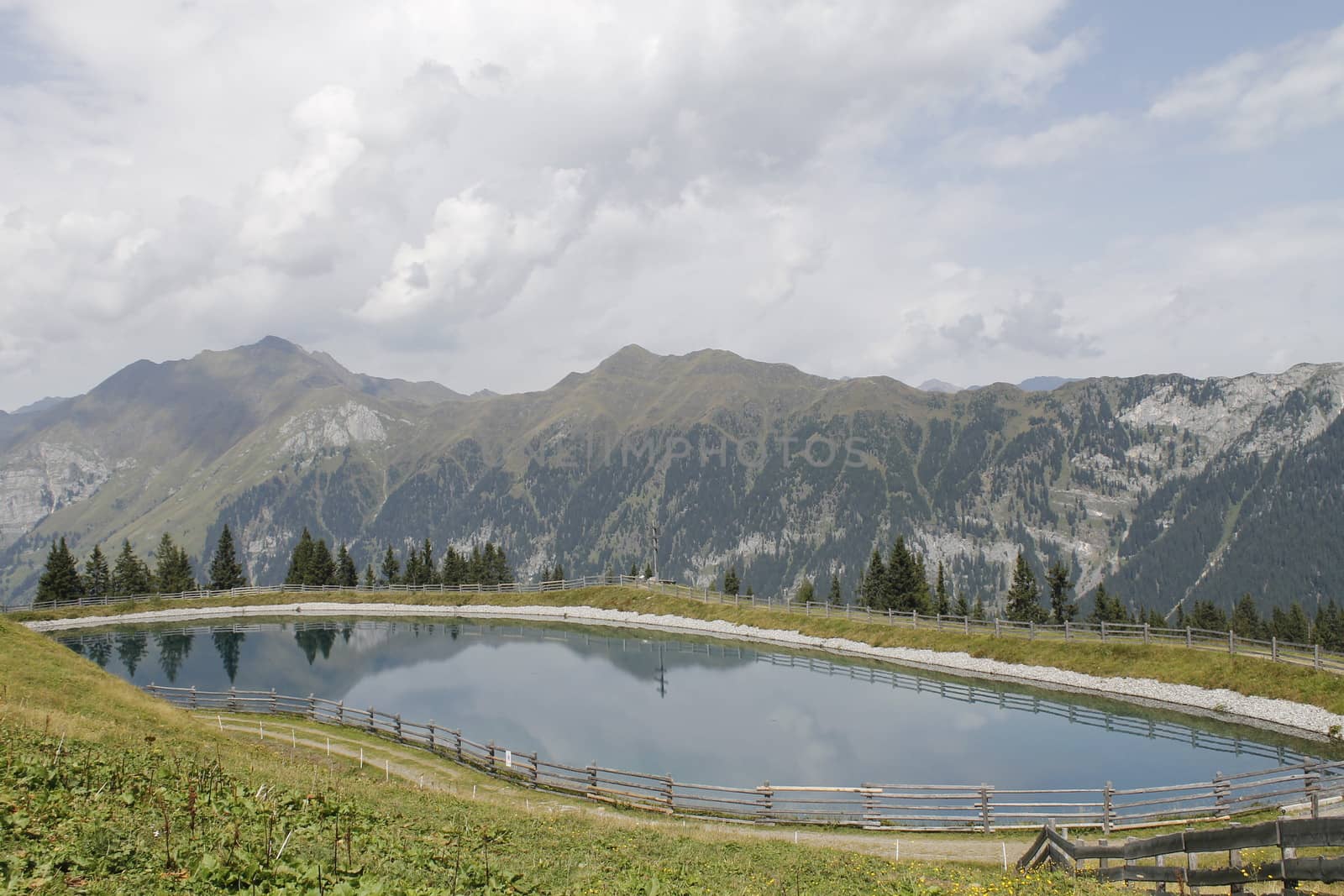 Scenic view to small alpine lake and big mountains with glacier in sunlight. Awesome green landscape with blue mountain lake among mosses in green highland valley in sunny day. Wonderful scenery.