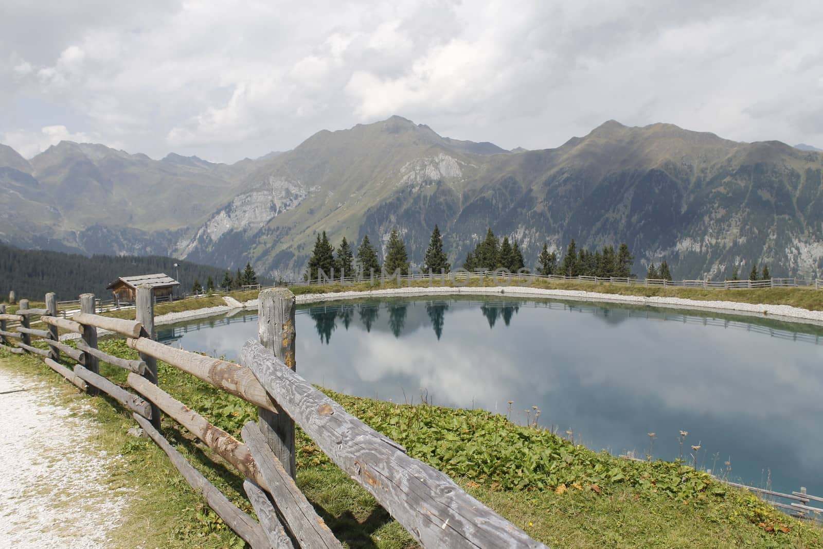 Scenic view to small alpine lake and big mountains with glacier in sunlight. Awesome green landscape with blue mountain lake among mosses in green highland valley in sunny day. Wonderful scenery.