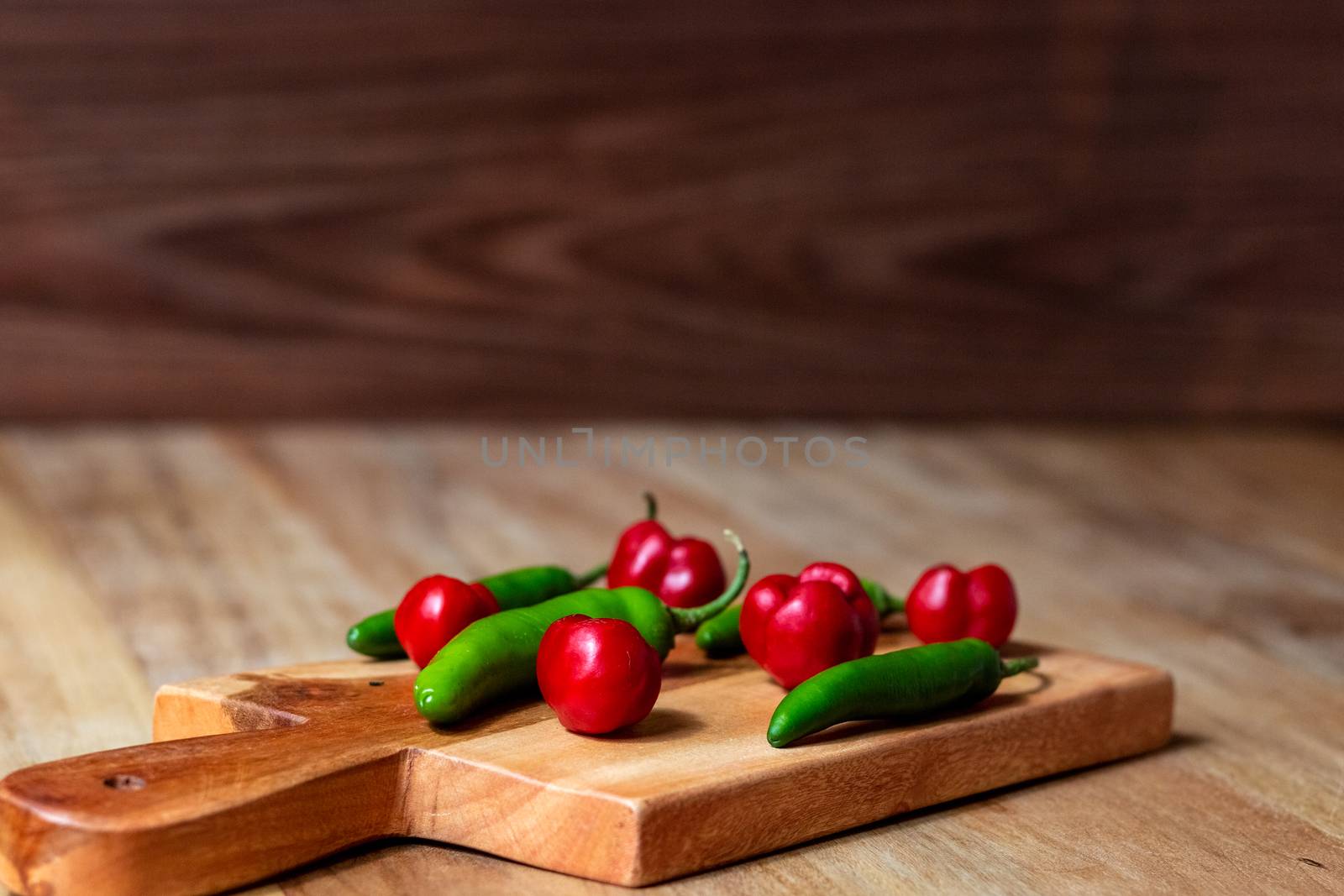 Apple and serrano peppers on chopping board on wooden surface. by leo_de_la_garza