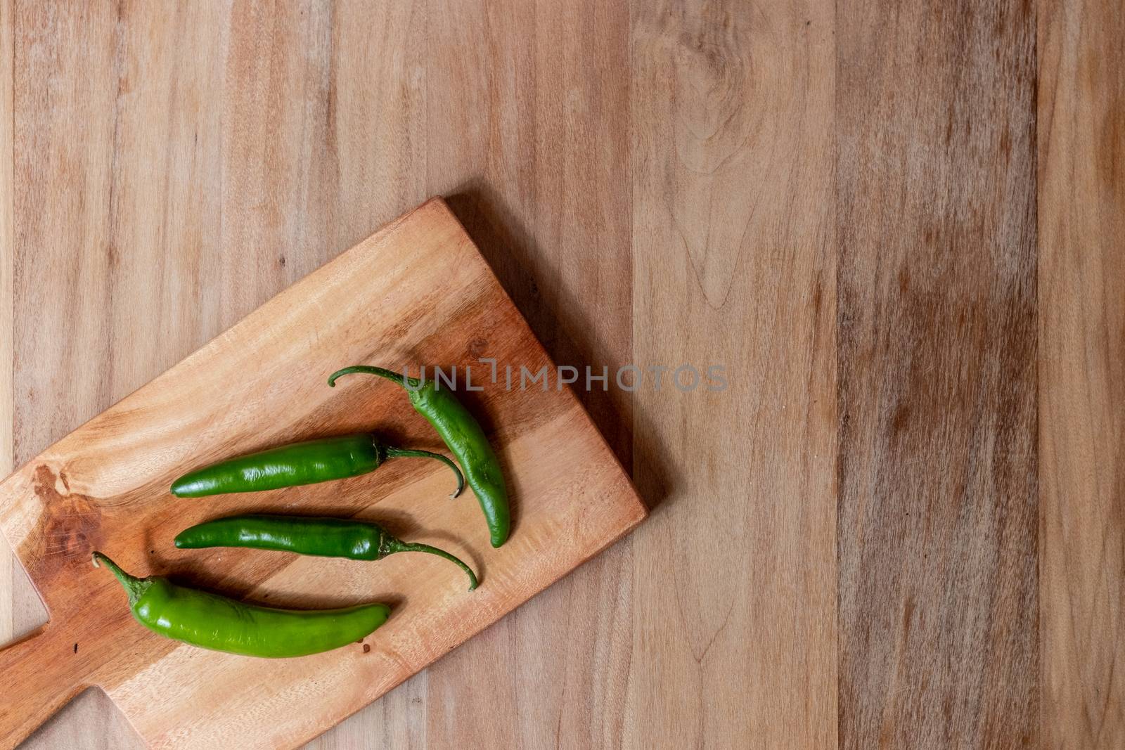 Apple and serrano peppers on chopping board on wooden surface. by leo_de_la_garza