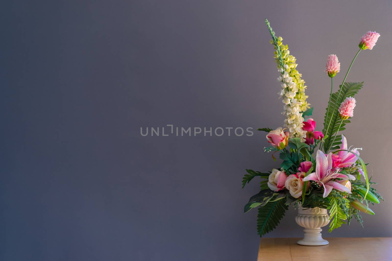 Fake flowers in a vase on wood table with gray background by domonite