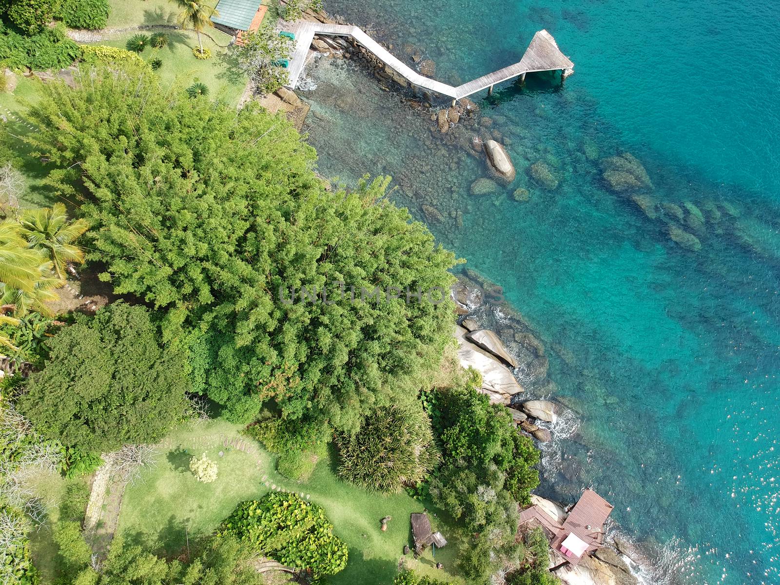 Aerial view of quiet little garden with wooden chairs between rocks and next to the ocean crystal clear water in tropical country. Brazil