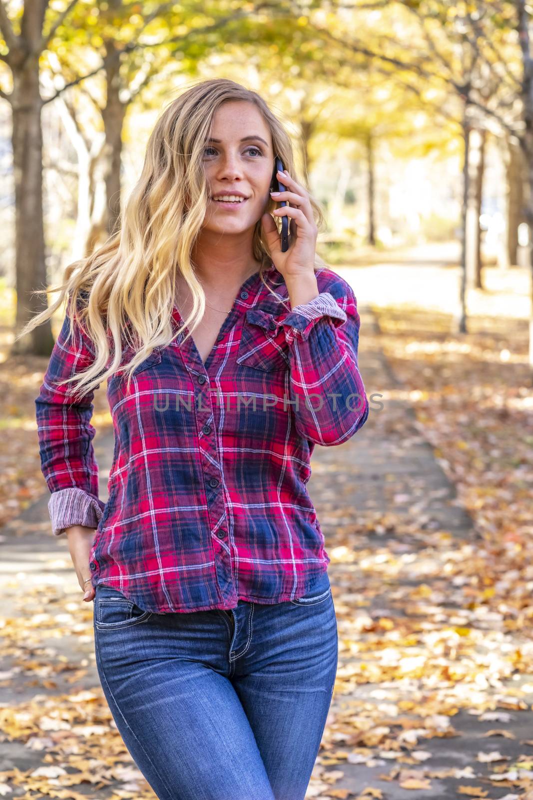 A gorgeous blonde model talks on her cellphone on an autumn day outdoors in a park