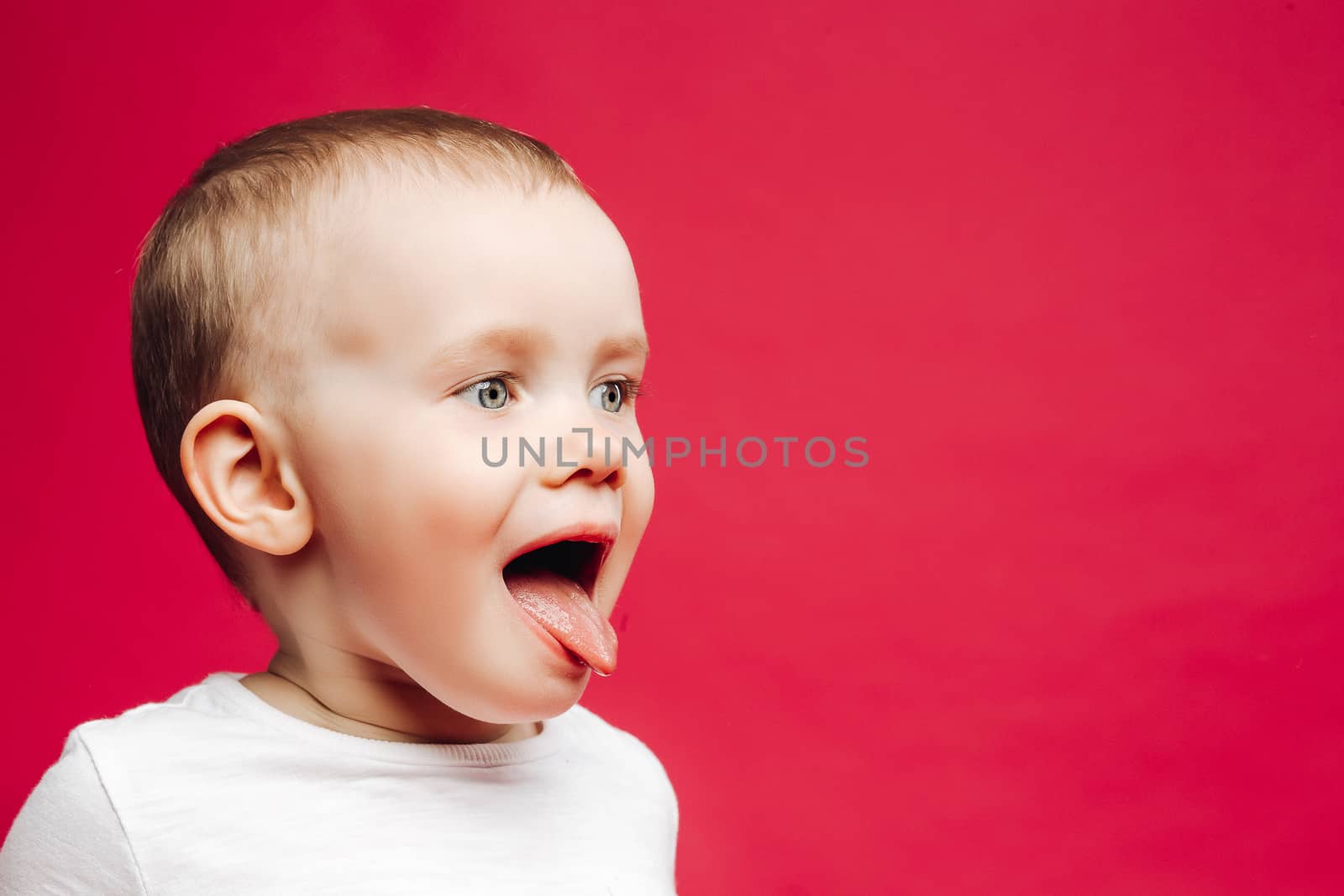 Portrait of little emotion boy playing at studio and showing tongue out. Sweet kid stick out and making face. Pink studio background.