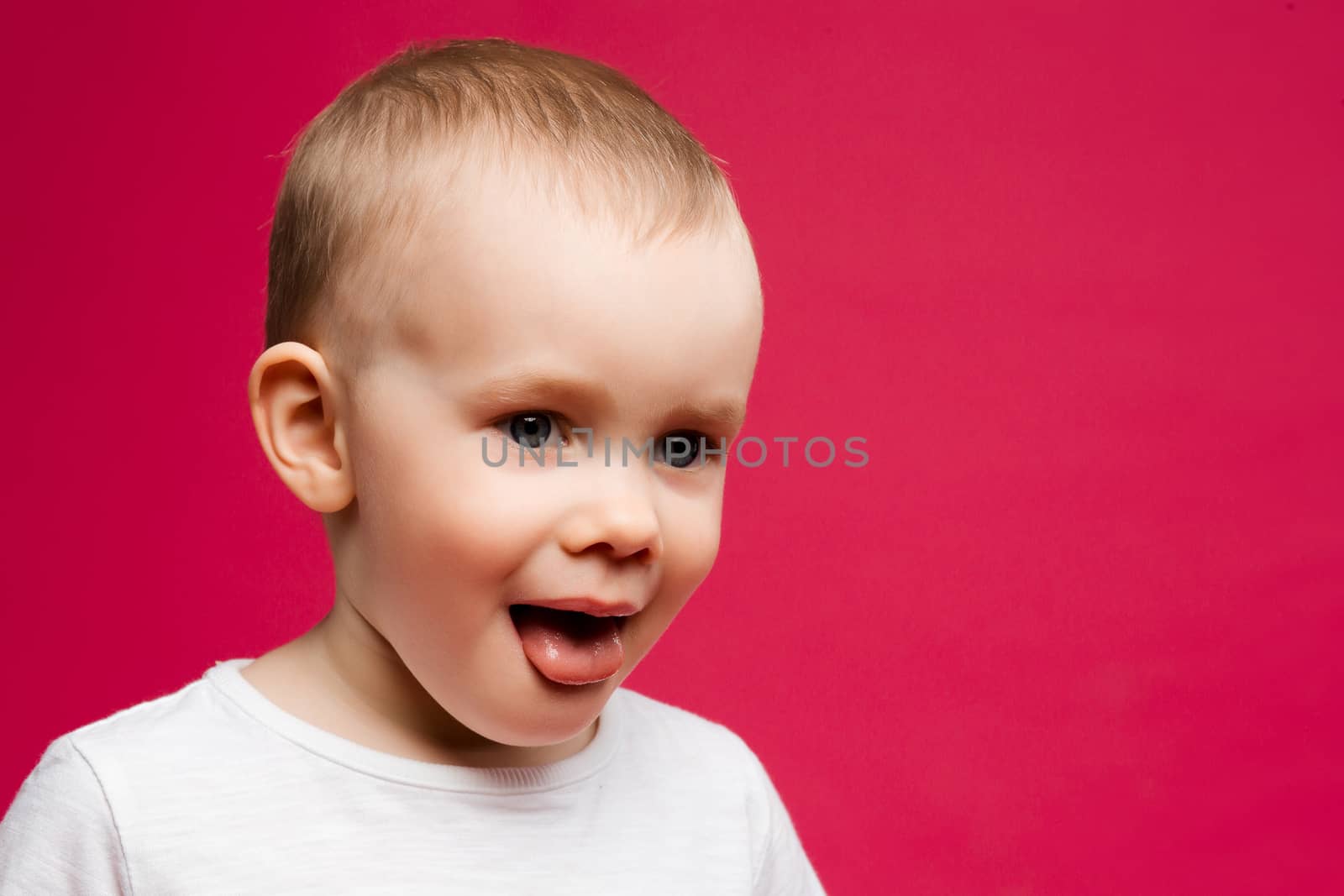 Emotion portrait of funny little boy with blue eyes showing tongue posing against pink background.Sweet child playing at studio and stick out. Pink background.