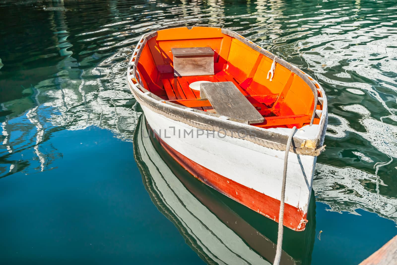 Bright orange and white painted wooden dinghy tied to pier by brians101