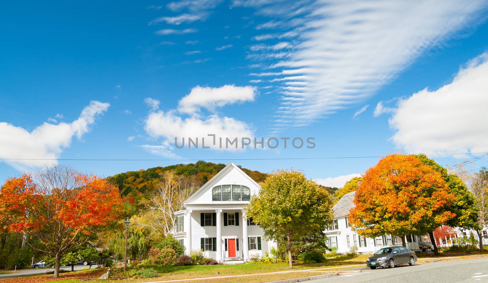 Street scene with traditional American white wooden residental architecture surrounded by brightly colored fall foliage and under blue sky.Newfane, Vermont, USA.