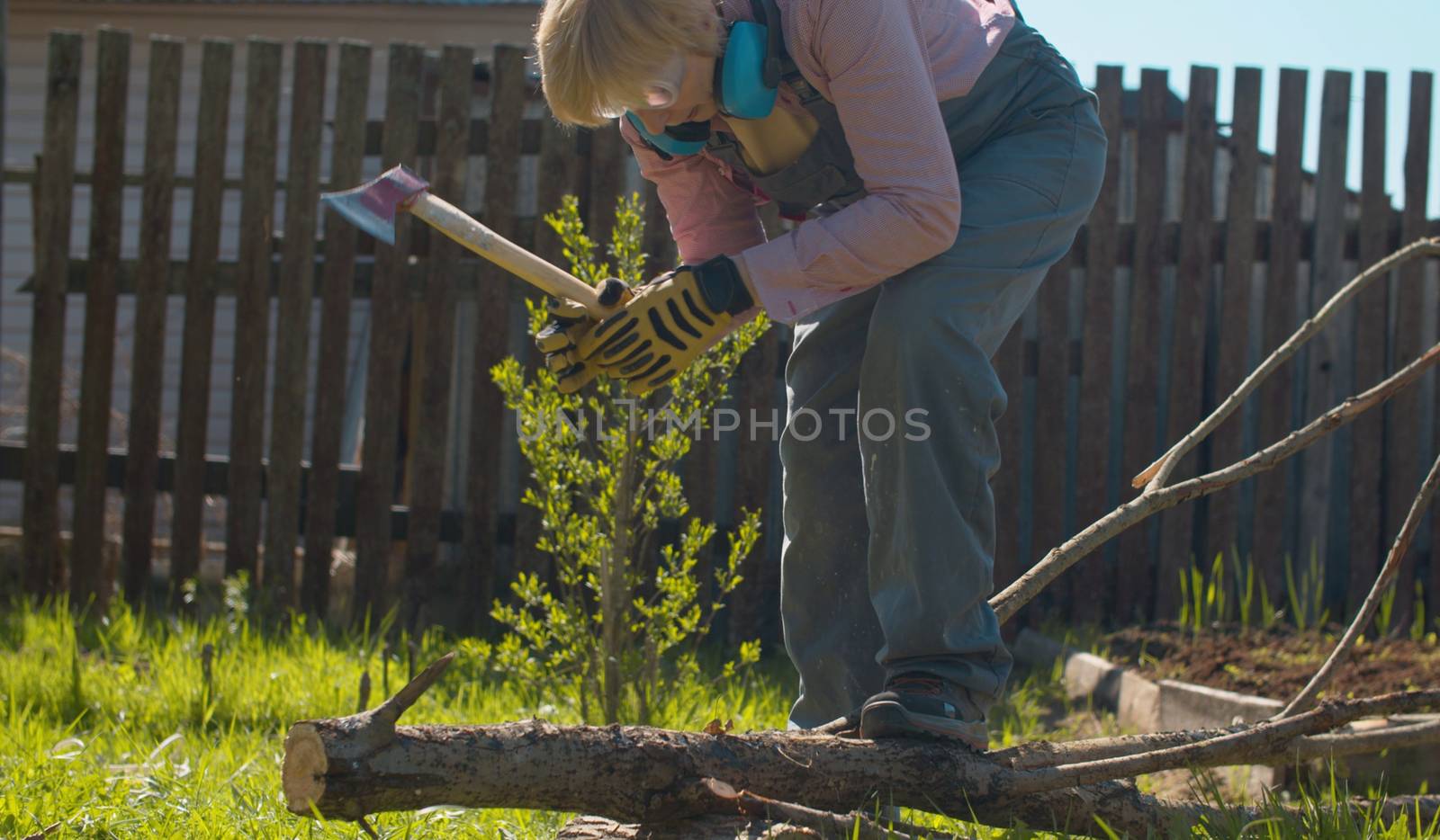Mature woman chopping branches of a tree with ax in the yard of a country house. Active and healthy lifestyle concept