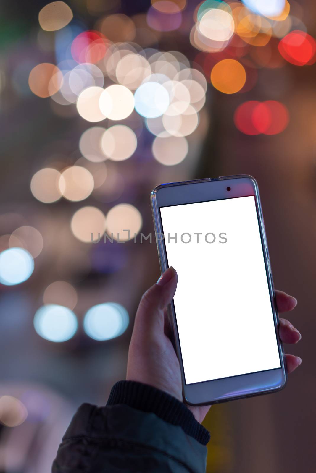 Woman holding a smartphone with a blank white screen at night with lights from car traffic in the background