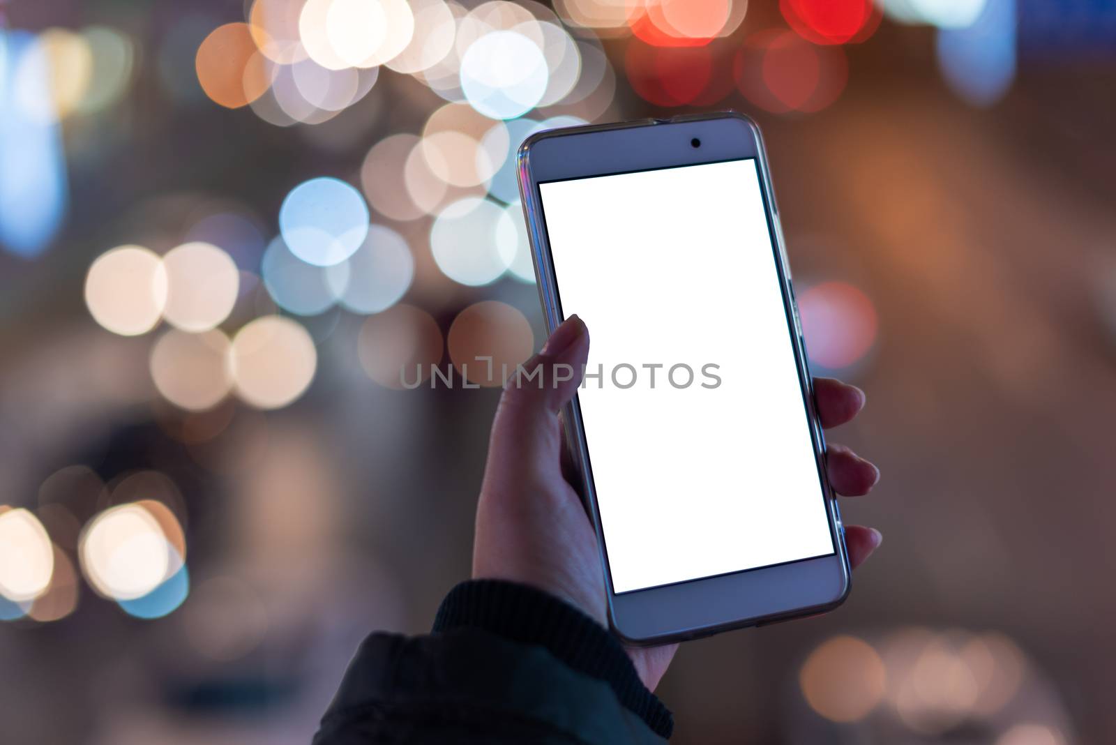 Woman holding a smartphone with a blank white screen at night with lights from car traffic in the background