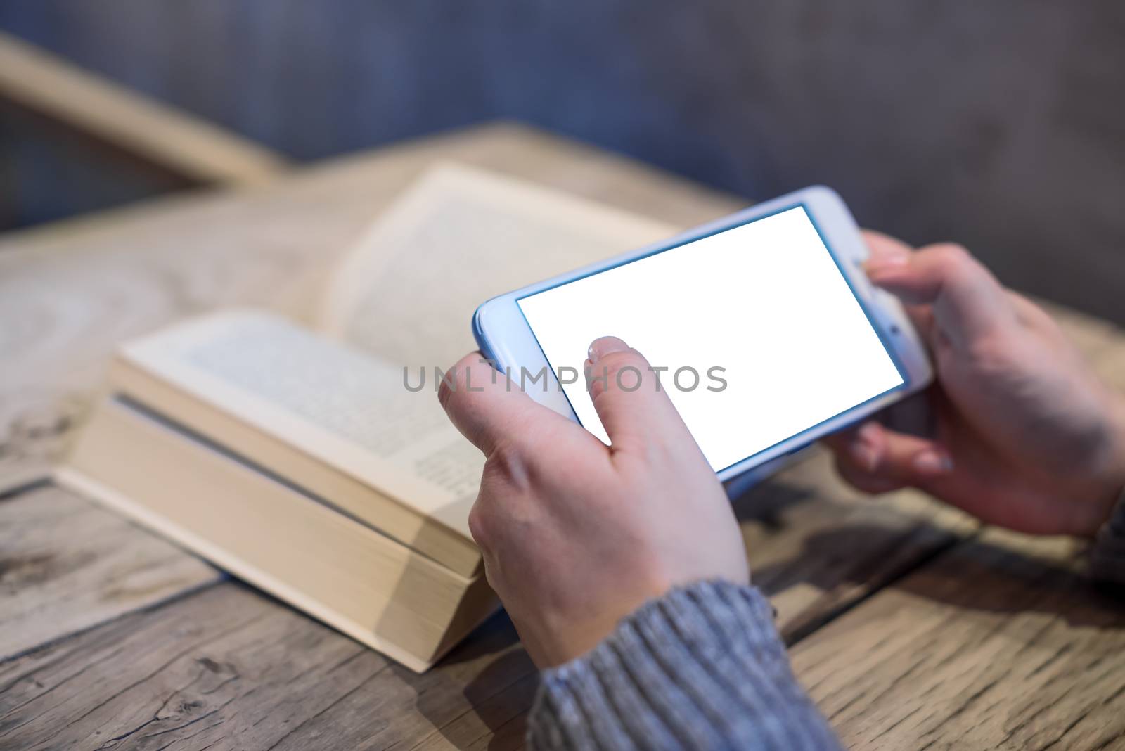 Woman holding a smartphone with an open book on a wooden table in a coffee shop