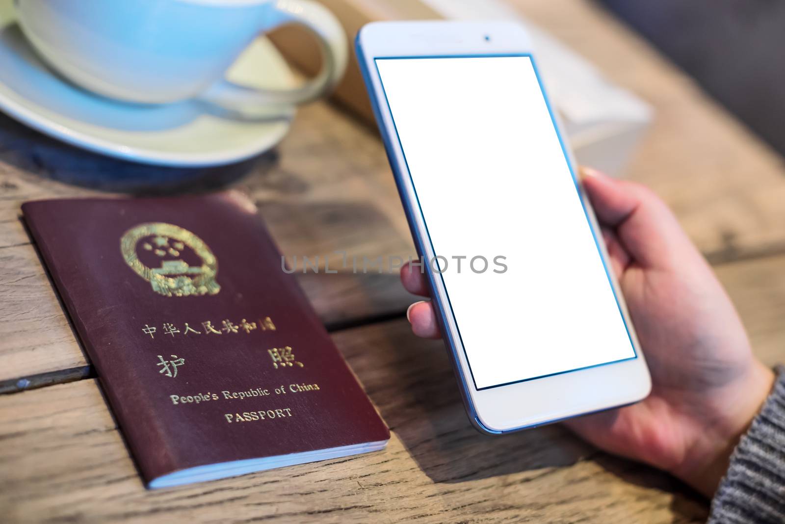 Woman holding a smartphone with a chinese passeport and coffee cup on a wooden table