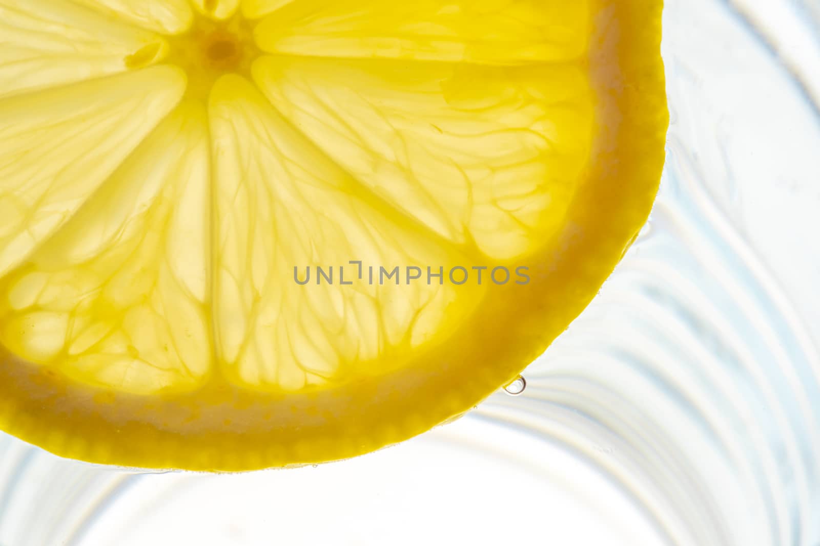 Lemon slice backlit in a glass of water close-up view