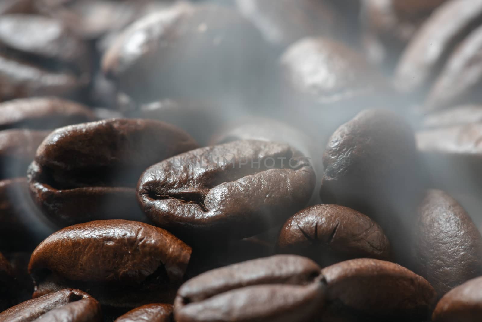 Heap of roasted coffee beans close-up view with smoke