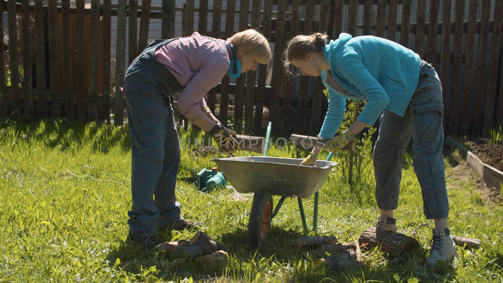 Two women working in the yard in spring. They putting firewood in a wheelbarrow. Active and healthy lifestyle concept