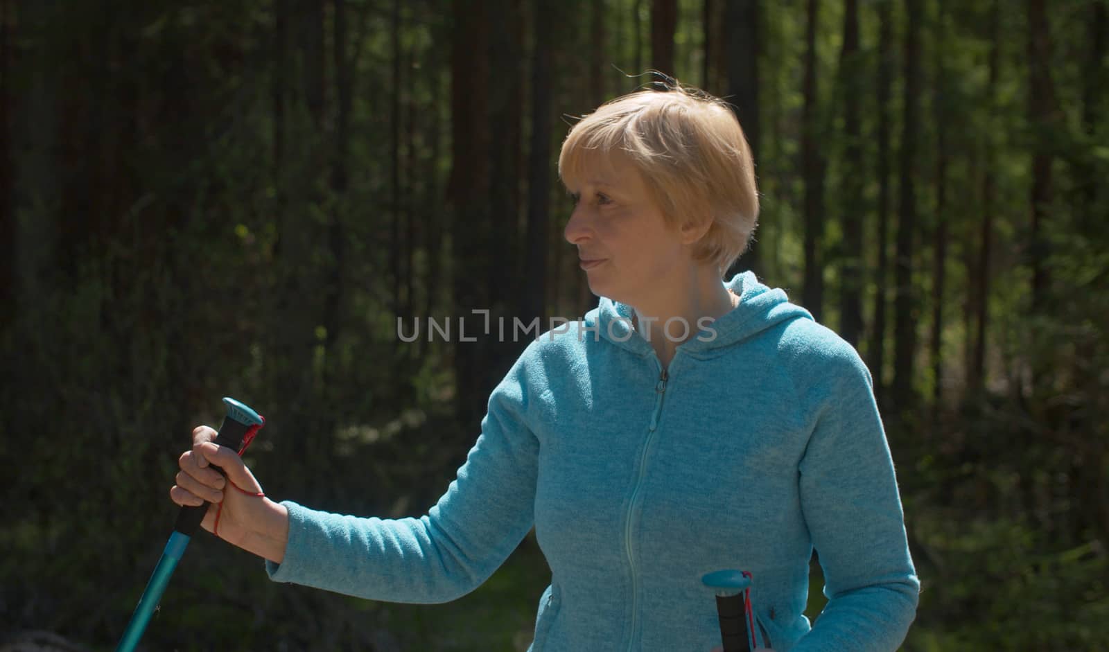 Close up portrait of mature blond woman in the forest with trekking poles. Trekking in the forest, active and healthy lifestyle concept