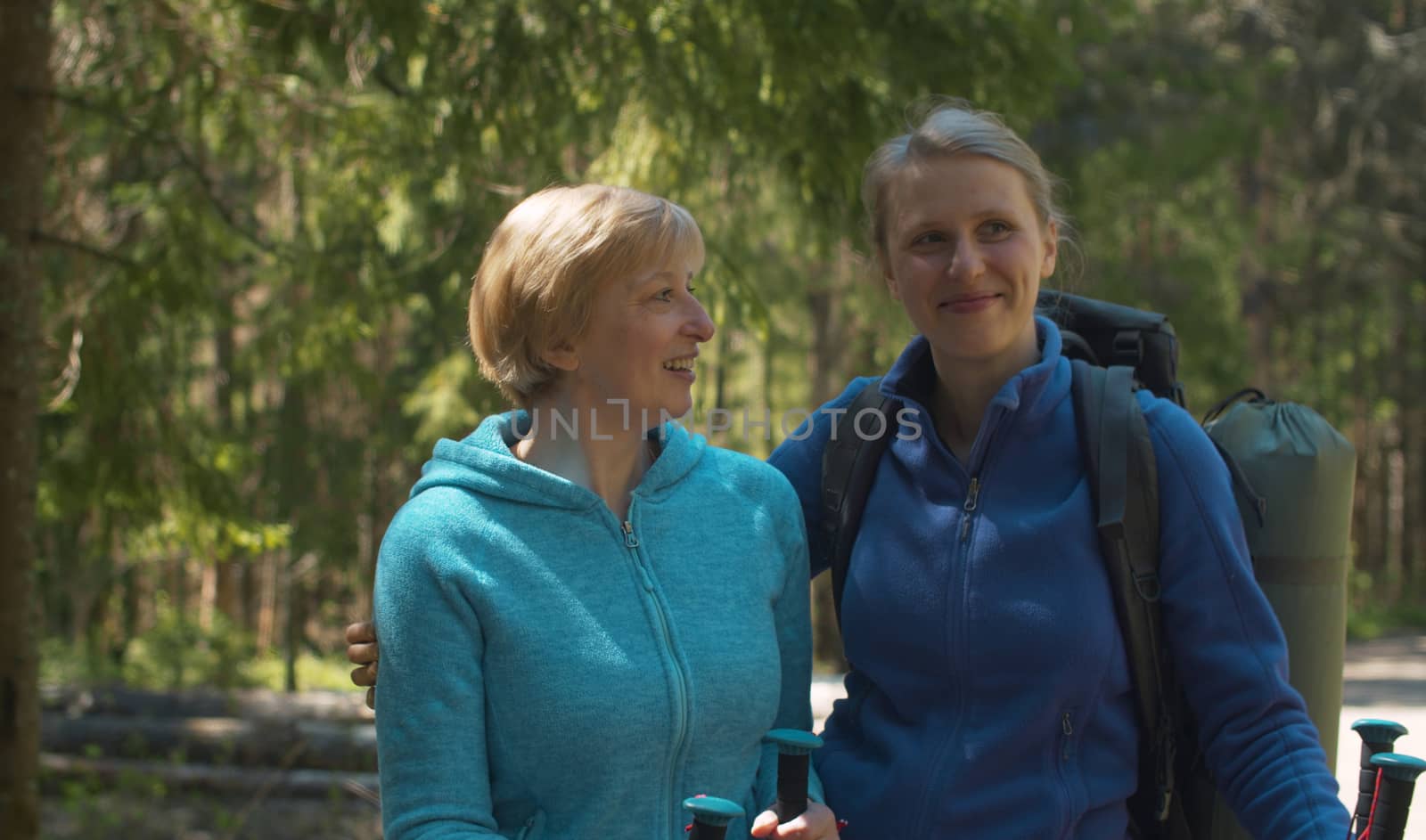 Close up portrait of young handsome woman with her mother in the forest. They are hugging, talking and smiling. Trekking in the forest, active and healthy lifestyle concept