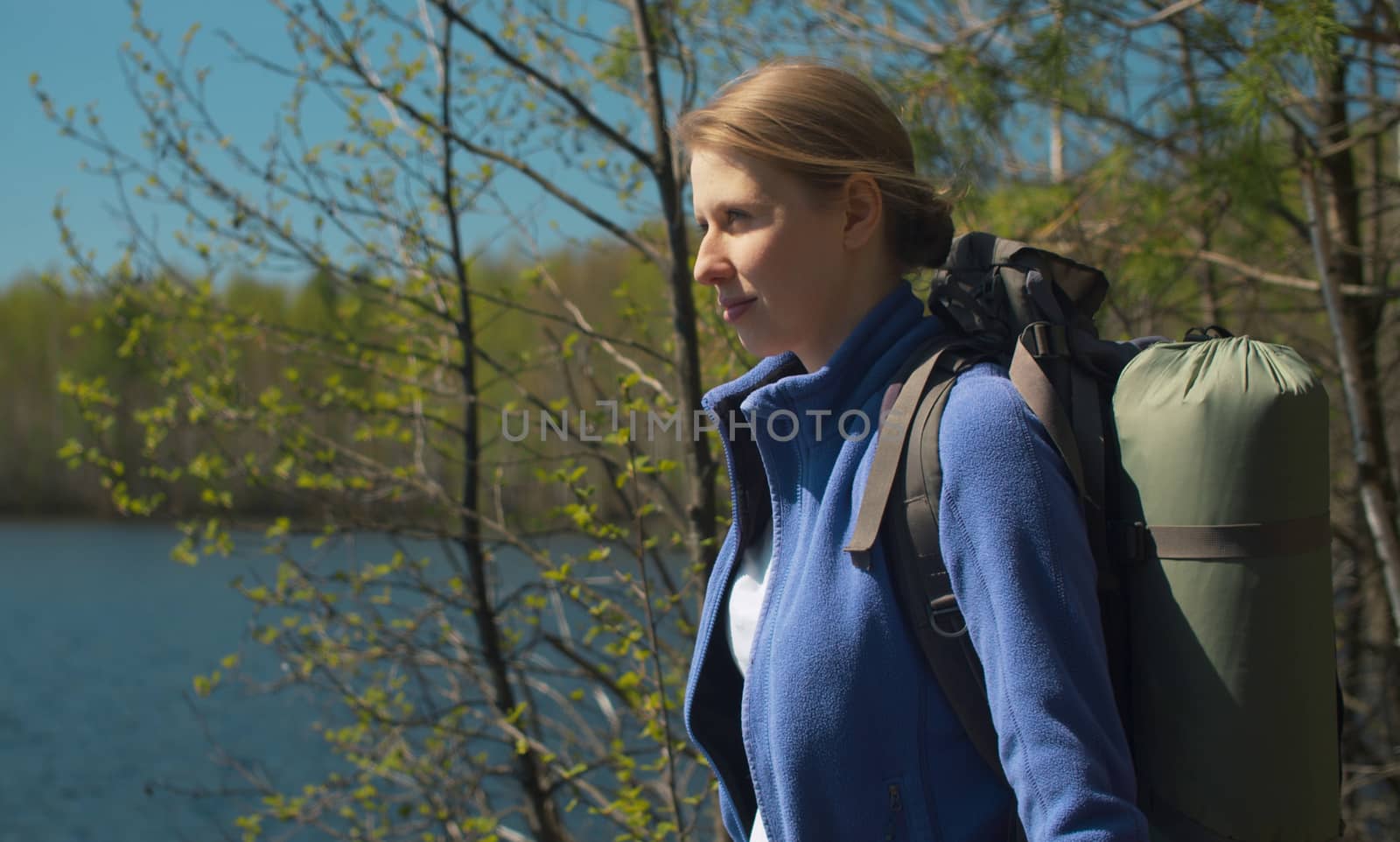 Portrait of young beautiful woman with a backpack on the shore of a forest lake. Trekking in the forest, active and healthy lifestyle concept