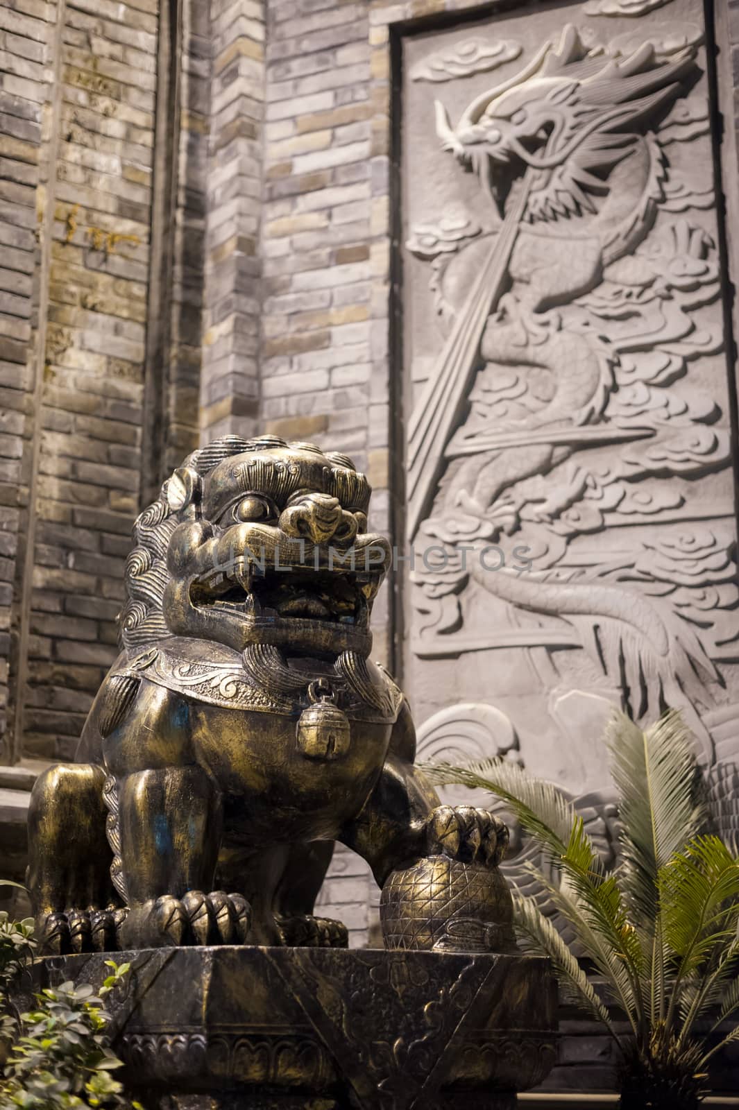 Lion bronze statue at with a dragon fresco on a brick wall at night in a chinese street in Chengdu, China