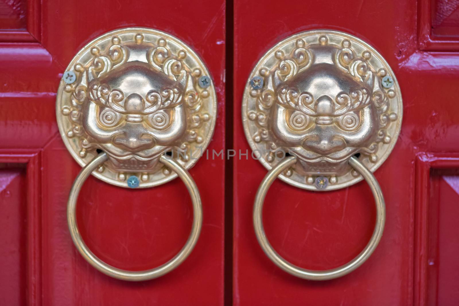 Golden colored chinese door knockers on a red door in China