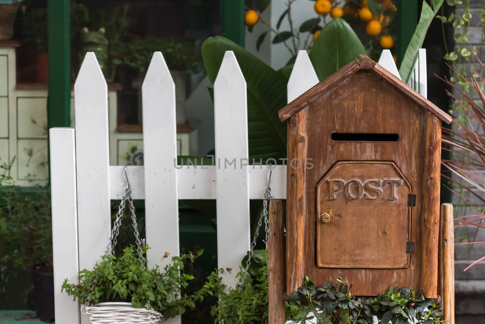 Wooden letter box with post inscription with plants and white fence in the background