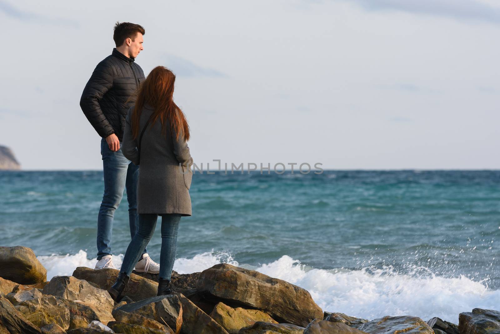 Two young people standing on a stone beach discussing the current situation.