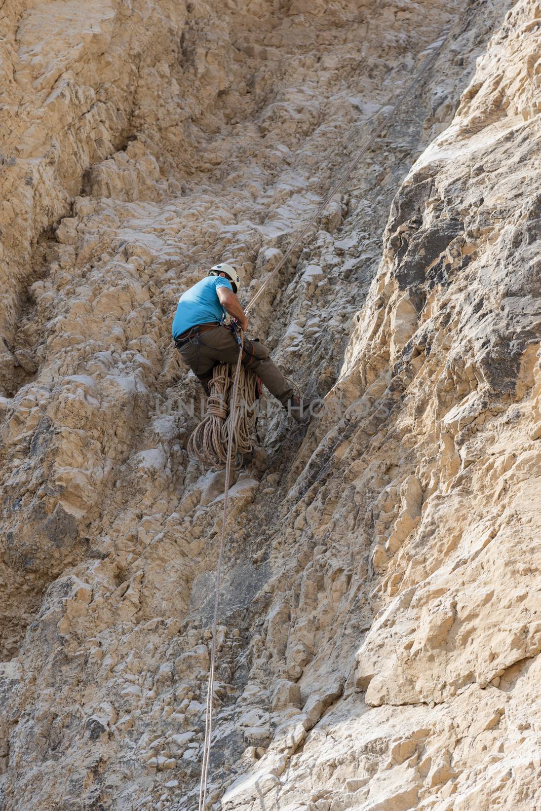 A man descends a high cliff in the desert, using rappelling. Abseiling Down Cliff. Cliff Rappel. High quality photo. Nahal Qumran