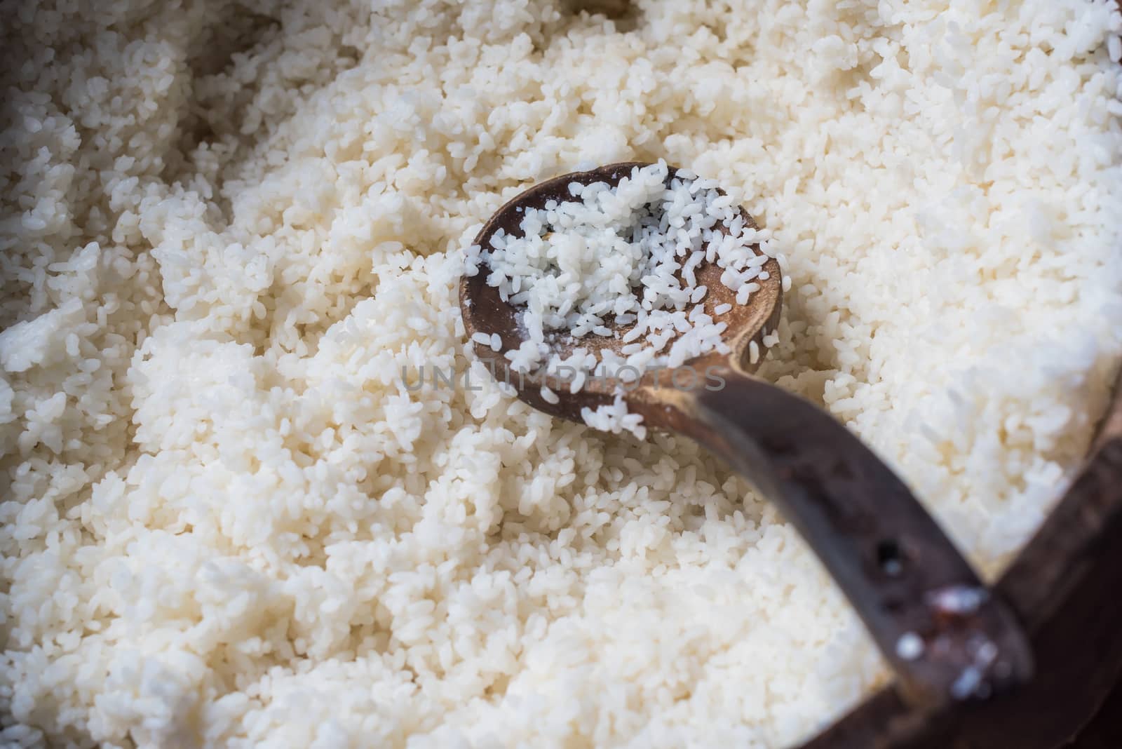 white rice in a large wooden container with a spoon