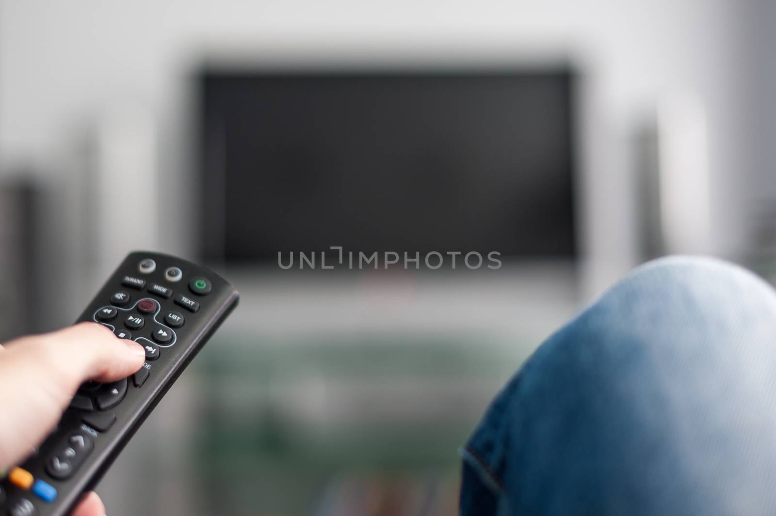 Man in blue jeans switching on a TV with a remote control