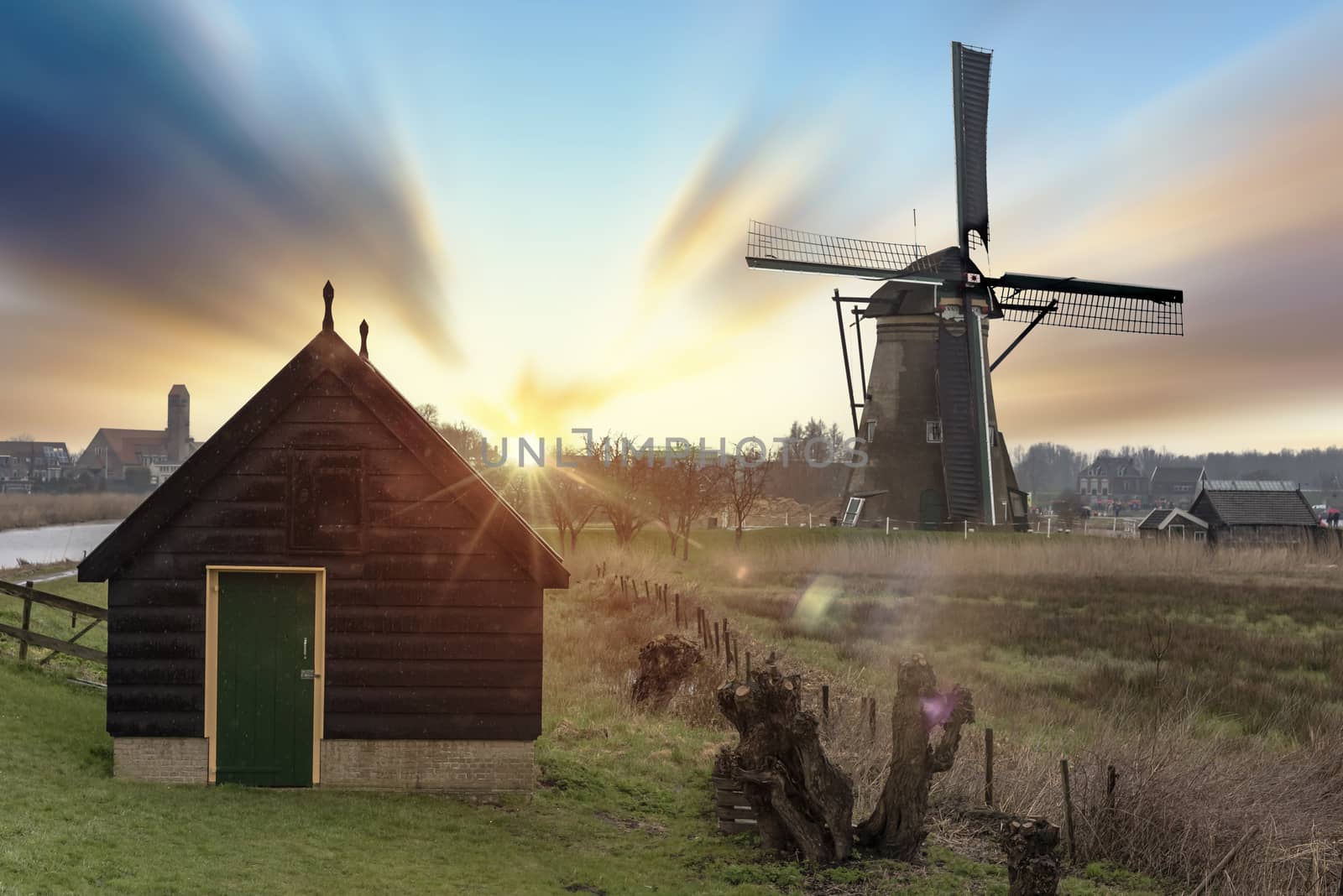 Long exposure of a typical vintage Dutch sunset landscape in the rural area of The Netherlands with windmill and low clouds by ankorlight